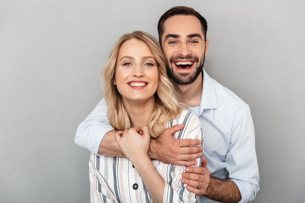 Primer plano de la foto de una linda pareja en ropa casual sonriendo y abrazándose unos a otros aislados sobre la pared gris