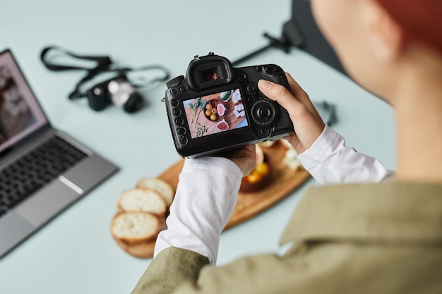 Primer plano de un fotógrafo de alimentos que trabaja en un estudio doméstico centrado en una cámara digital con una imagen en el espacio de copia de la pantalla