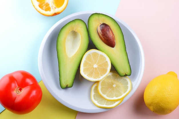 Primer plano de fruta verde saludable con cítricos y tomate rojo sobre un fondo colorido Dos mitades de un aguacate maduro con semilla con una rodaja de limón en un plato blanco Concepto de comida vegetariana