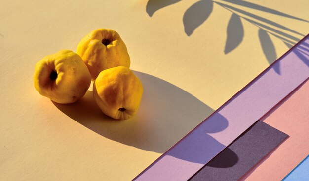 Primer plano de frutos maduros de membrillo japonés dulce en papel en capas geométricas de color rosa y amarillo.