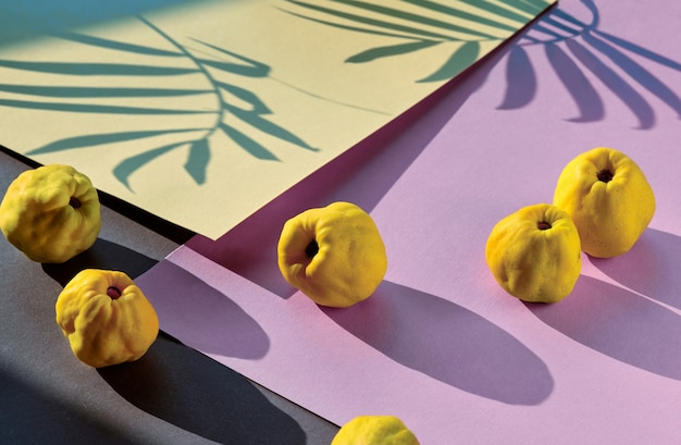 Primer plano de frutos maduros de membrillo japonés dulce en papel en capas geométricas de color rosa y púrpura.