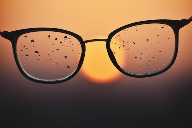 Foto primer plano de gafas mojadas contra el cielo durante la puesta de sol