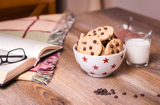 Foto primer plano de galletas con chispas de chocolate en el tazón de estrellas y vaso de leche sobre un fondo de madera