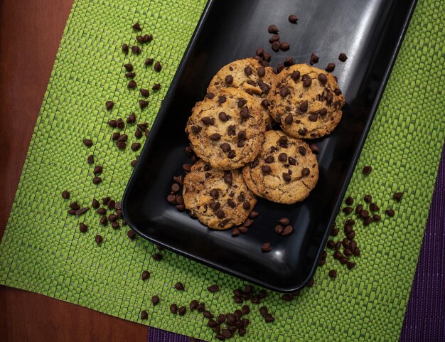 Primer plano de galletas con trocitos de chocolate sobre manteles de colores dentro de una placa negra