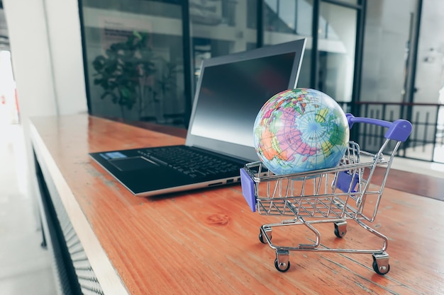 Primer plano del globo en el carrito de compras por computadora portátil en la mesa