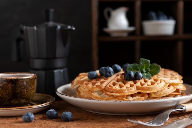 Primer plano de gofres vieneses suaves con arándanos, una taza de café y una cafetera