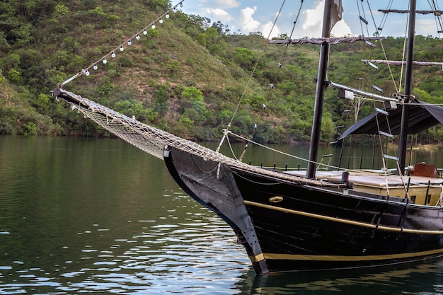 Primer plano de una goleta negra navegando en un lago tranquilo con montañas al fondo