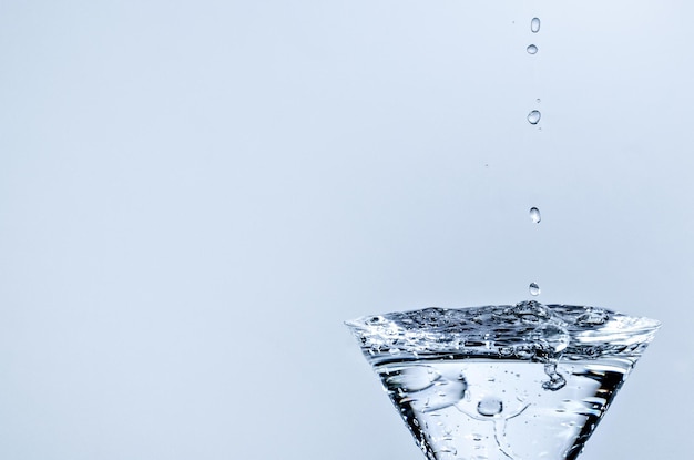 Primer plano de una gota de agua cayendo en un vaso sobre fondo blanco.