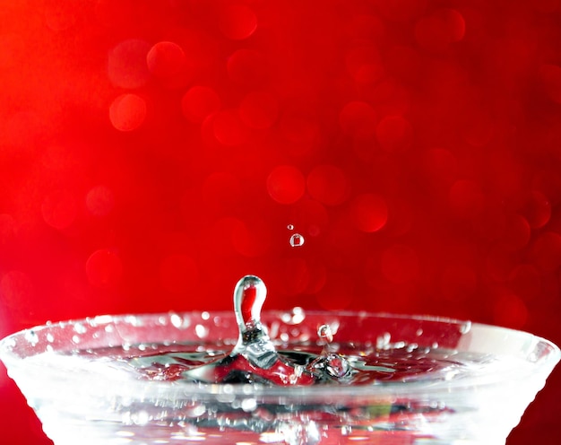 Primer plano de una gota de agua cayendo en un vaso sobre fondo rojo.