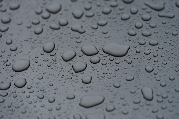 Primer plano de las gotas de lluvia sobre el capó negro del fondo del coche