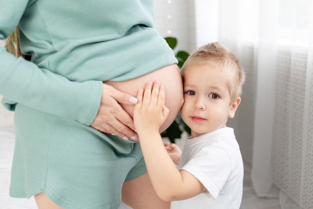 Primer plano de una gran barriga de una mujer embarazada y un bebé abrazando el vientre de una madre, el concepto de esperar un hijo, el amor y la crianza