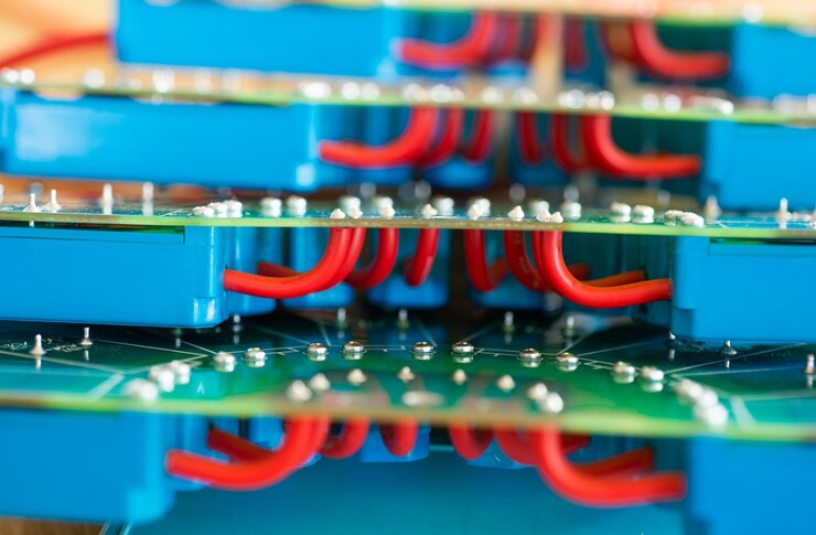Foto primer plano de un gran microcircuito verde con cables rojos de alto voltaje y relés azules conectados a él en una fábrica de equipos militares. el concepto de nuevas tecnologías de alta tensión en producción