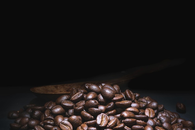 Primer plano granos de café en una cuchara de madera sobre fondo negroMacro