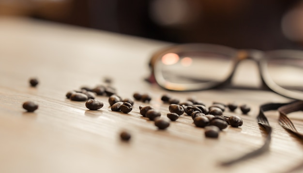 Primer plano de granos de café sobre la mesa con vasos en el fondo con espacio de copia