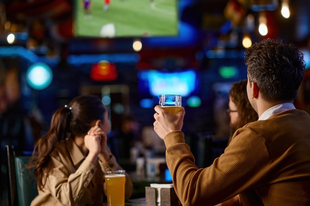 Primer plano del grupo de amigos brindando con cerveza mientras están sentados juntos en un pub de cerveza