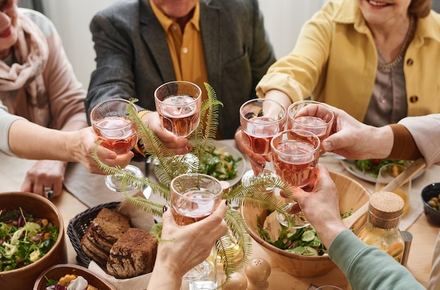 Primer plano de un grupo de personas sosteniendo vasos con vino tinto y brindando durante la cena en la mesa