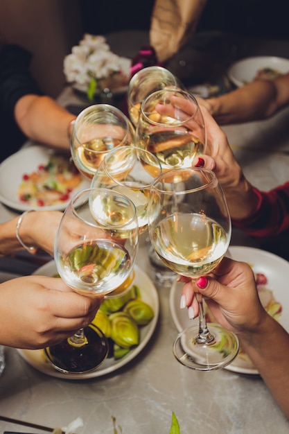 Primer plano de un grupo de personas tintineando copas con vino o champán frente a bokeh