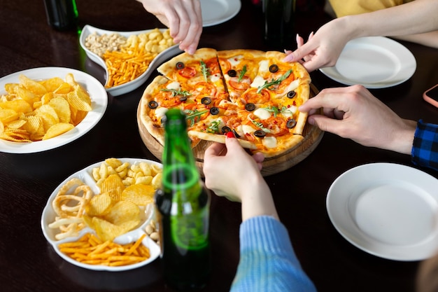 El primer plano de guapos jóvenes amigos bebe cerveza y come pizza en el pub