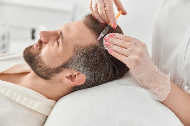 Foto primer plano hace inyecciones de mesoterapia a un hombre joven. tratamiento de esteticista masculino para tensar y suavizar las arrugas de la piel de la cara.