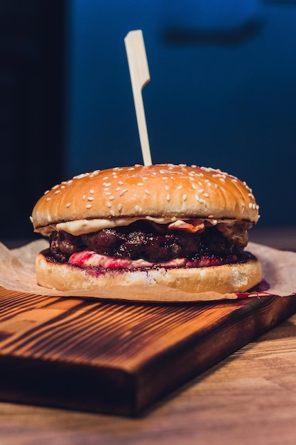 Primer plano de hamburguesa apilada con coberturas frescas en panecillo artesanal de grano entero en superficie de madera rústica