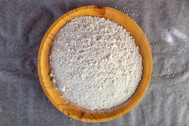 Primer plano de harina de trigo blanco desmenuzable en un plato de madera en la mesa de la cocinaLay Flat