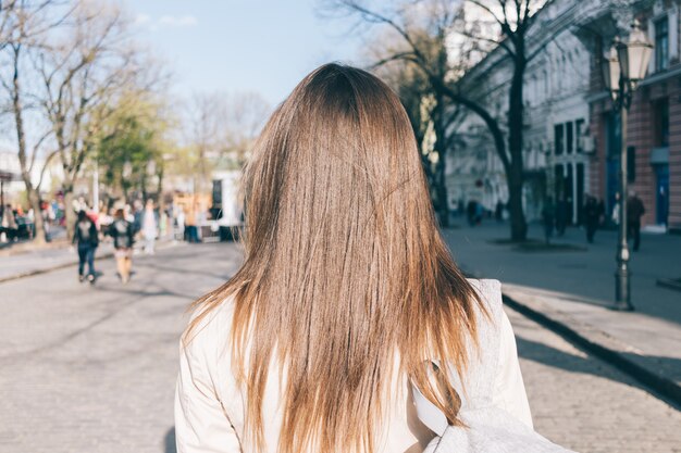 Primer plano de una hermosa chica morena con cabello largo en un abrigo recorre la ciudad en primavera