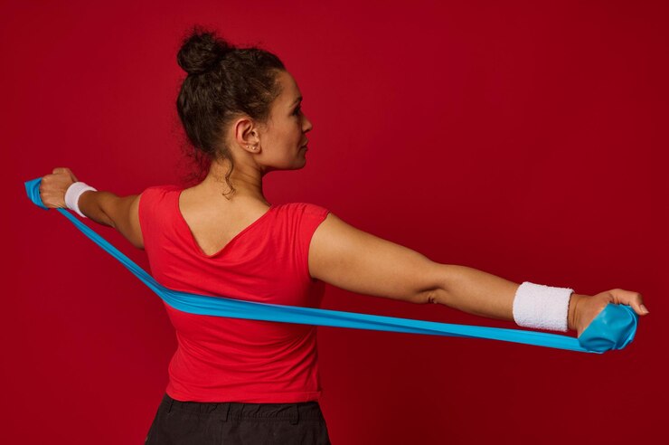 Foto primer plano de una hermosa deportista hispana que trabaja con una correa de goma elástica contra un fondo de color rojo con espacio para anuncios de copia