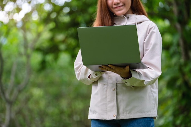 El primer plano de una hermosa joven asiática sosteniendo y usando una computadora portátil al aire libre