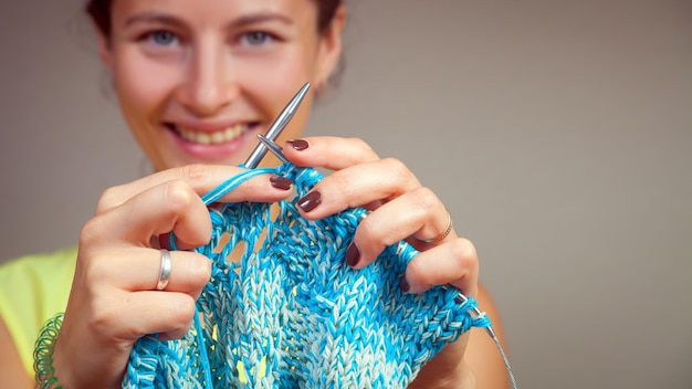 Primer plano de una hermosa mujer de cabello oscuro sonriendo y tejiendo con agujas de tejer