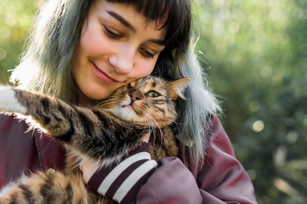 Primer plano de una hermosa mujer sonriente abrazando a su gato atigrado en el jardín