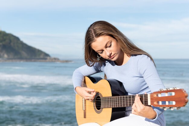 Primer plano de un hermoso músico adolescente tocando la guitarra en la playa