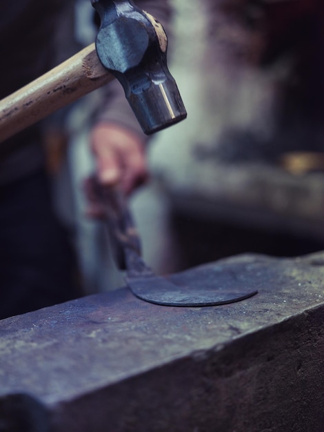 Primer plano de un herrero anónimo usando un martillo mientras forja metal sobre un viejo yunque en un taller tradicional