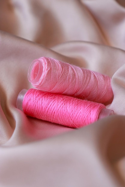 primer plano de un hilo de bobina de coser rosa sobre textiles de seda