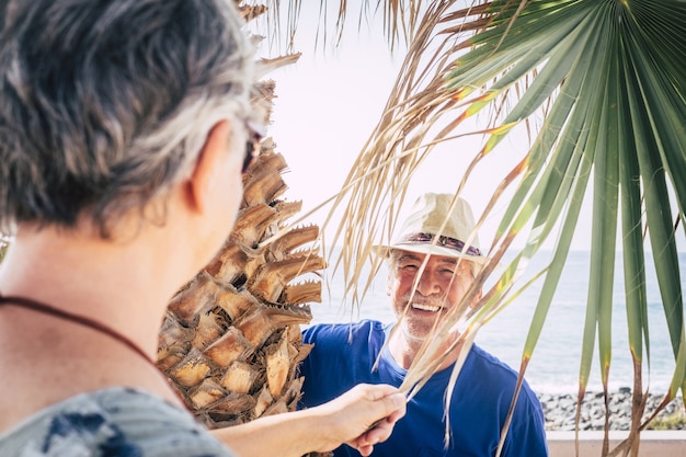 Primer plano de un hombre de 70 años riendo bajo una palmera jugando al escondite. Vacaciones, concepto de diversión