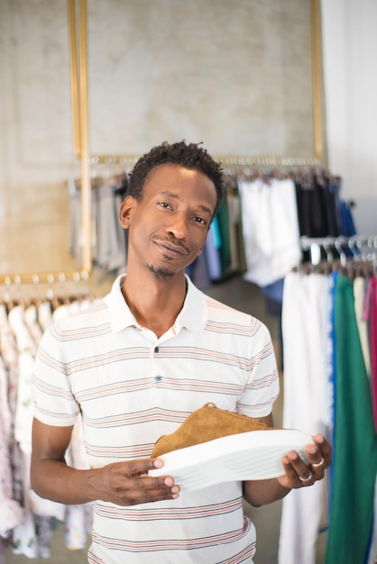 Primer plano de un hombre afroamericano sosteniendo zapatos para hombres en la tienda. Joven comprando ropa de hombre en boutique eligiendo zapatos nuevos modelos mirando a la cámara. Moda de ropa de hombre, estilo casual, concepto de compras.