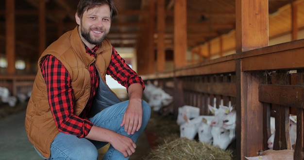 Primer plano hombre agricultor dando heno fresco a la cabra de pie puesto de granero Empleado de la granja alimentando el rebaño de ganado de las manos en tierras de cultivo Agrónomo cuidando animales domésticos en la granja de cabras moderna