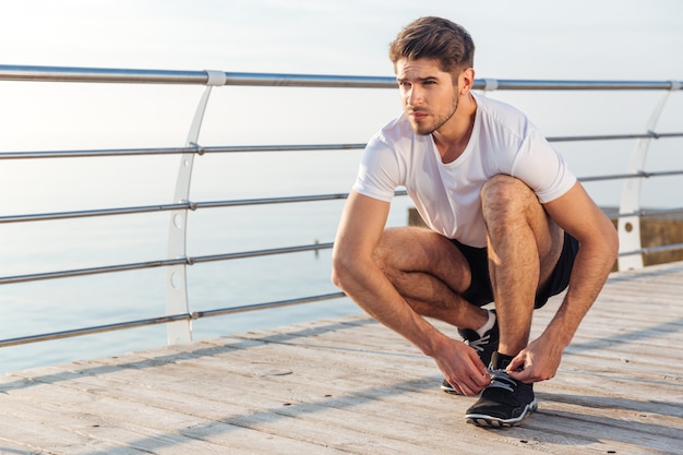 Primer plano de un hombre atleta ata sus zapatillas de deporte en el muelle