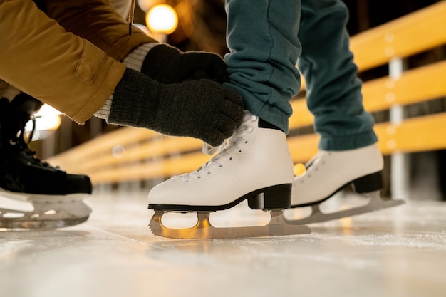 Primer plano del hombre ayudando a su novia a atar los cordones de los zapatos en patines antes de patinar