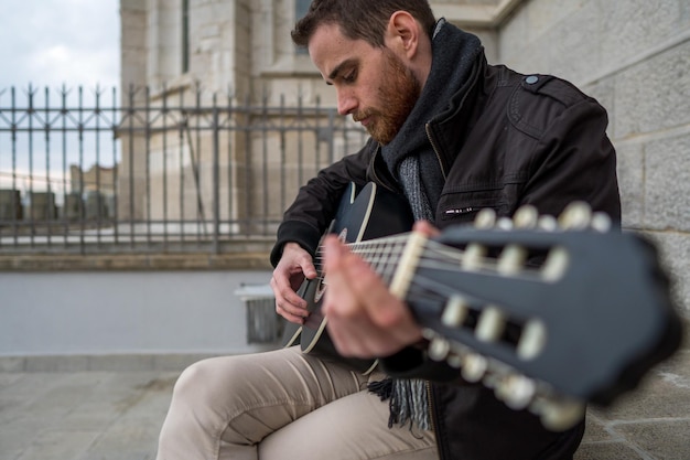 Primer plano de un hombre con barba roja aprendiendo a tocar la guitarra solo en una plaza vacía