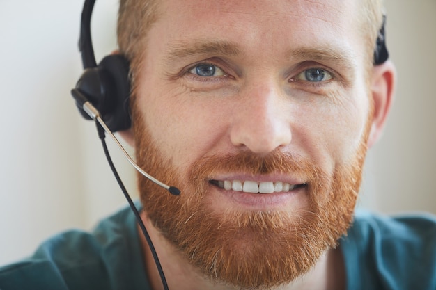 Primer plano de hombre barbudo en auriculares sonriendo mientras trabaja en call center