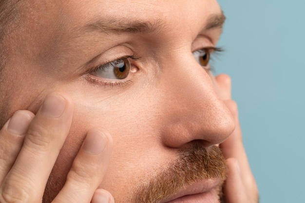 Primer plano de un hombre barbudo serio mirando las arrugas debajo de los ojos tocando la piel de la cara cuidado de la piel después de los 40 años