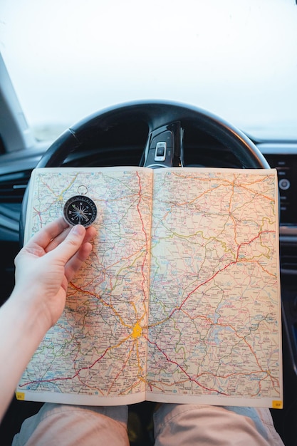 Primer plano de un hombre con una brújula y un mapa en sus manos dentro de un coche
