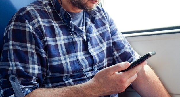 Primer plano de un hombre con una camisa a cuadros azul sentado en el metro escuchando música con auriculares