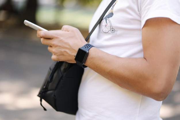 Primer plano de un hombre en camiseta blanca con bolso shouler negro usando teléfono outddor hombre tiene reloj inteligente