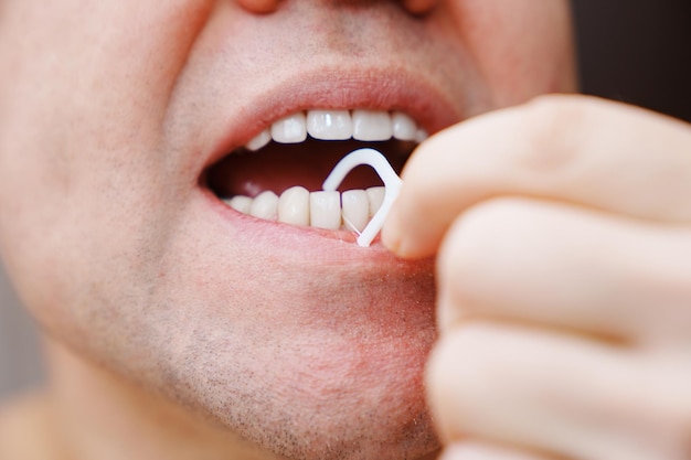 Primer plano un hombre cepillarse los dientes palillo de plástico con hilo dental