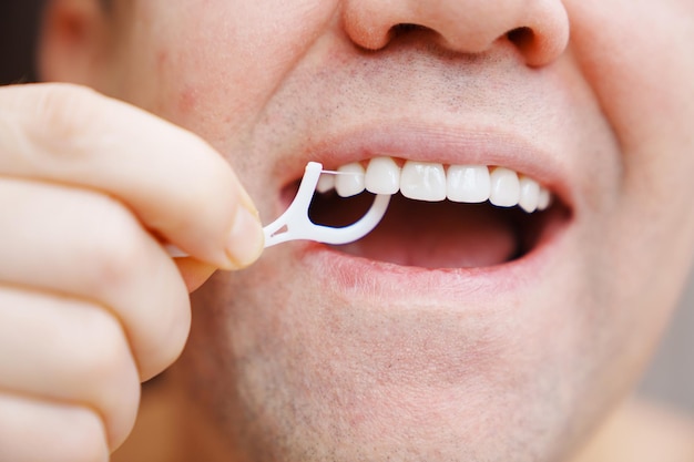 Primer plano un hombre cepillarse los dientes palillo de plástico con hilo dental