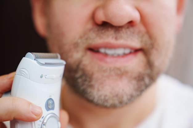 Primer plano de un hombre con cerdas sosteniendo una maquinilla de afeitar eléctrica