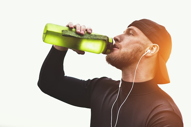 Primer plano hombre deportivo barbudo tomar un descanso y beber un agua después de la sesión de entrenamiento.