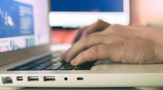 Primer plano de un hombre escribiendo en el teclado de una computadora portátil