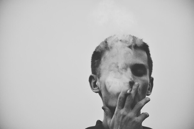 Primer plano de un hombre fumando un cigarrillo contra un cielo despejado